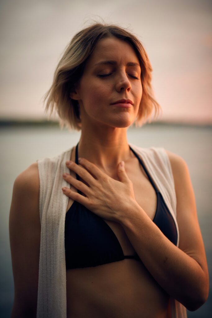 Woman with eyes closed hand on heart near water